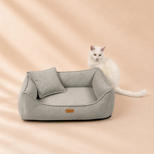 Weiße Katze sitzt hinter dem orthopädischen Katzenbett FINE CORD in Hellgrau