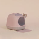 Katze hinter der Design-Katzentoilette ‚Minù‘ – modernes Katzenklo in Rosa mit integriertem Filter.